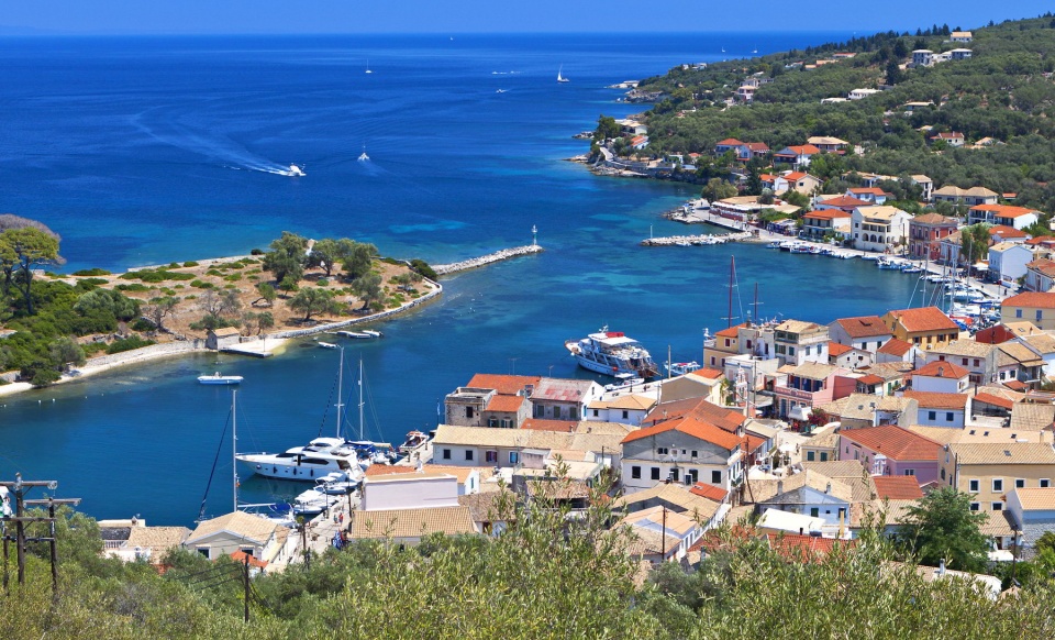 Charming Greek harbor village with traditional red-roofed buildings and yachts in turquoise waters